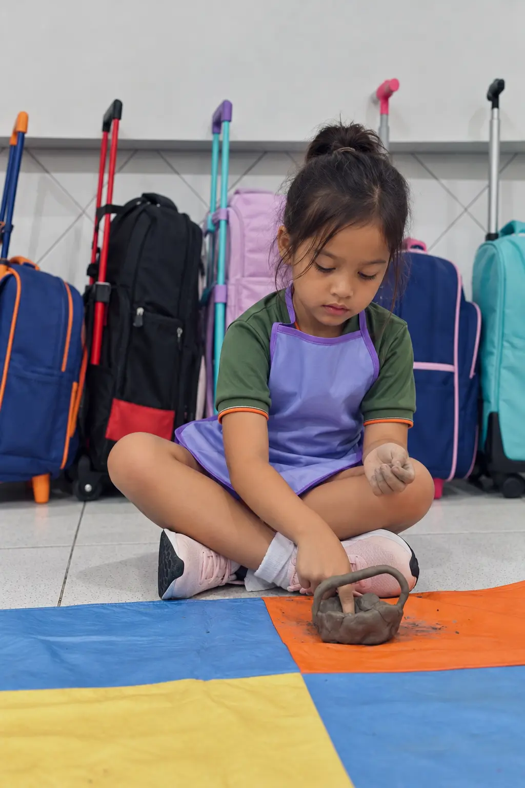 Aluna da Educação Infantil do Colégio CEA, de farda verde e avental lilás, modelando argila sobre um tapete colorido