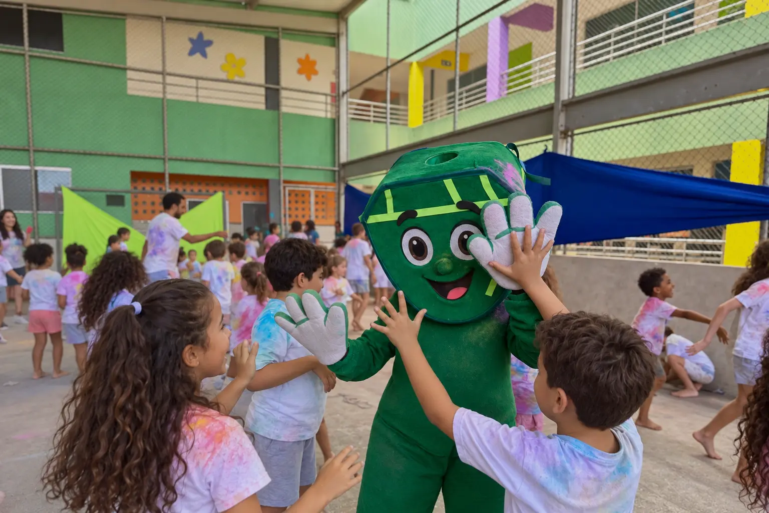 Festa das Cores no pátio do Colégio CEA: crianças com camisetas coloridas de pó brincando com o mascote verde da escola